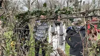 5 personnes derrière des plantes suspendues à l'horizontal, comme des vignes